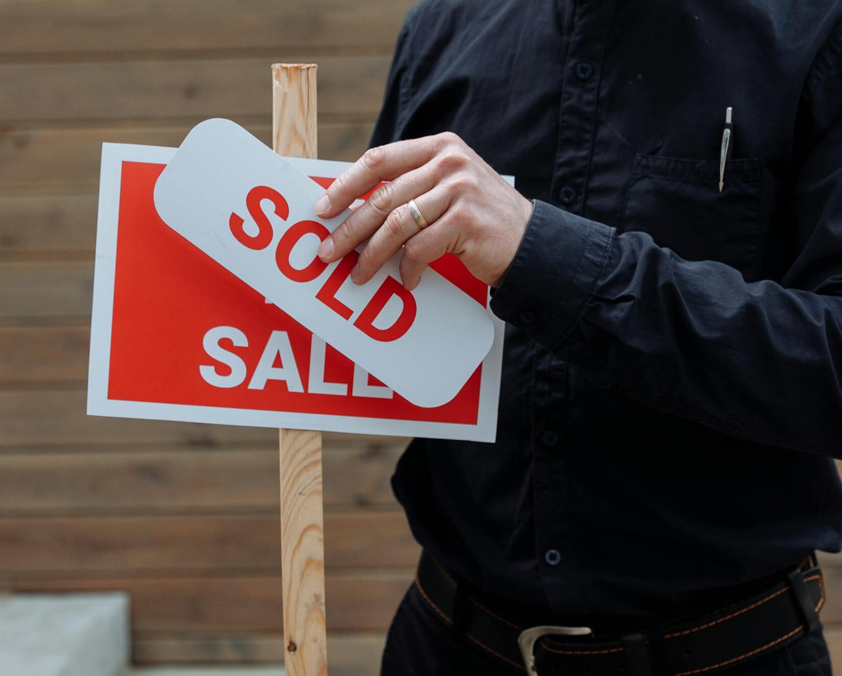 A real estate agent placing a sold sticker over a sale sign, indicating successful property deal.